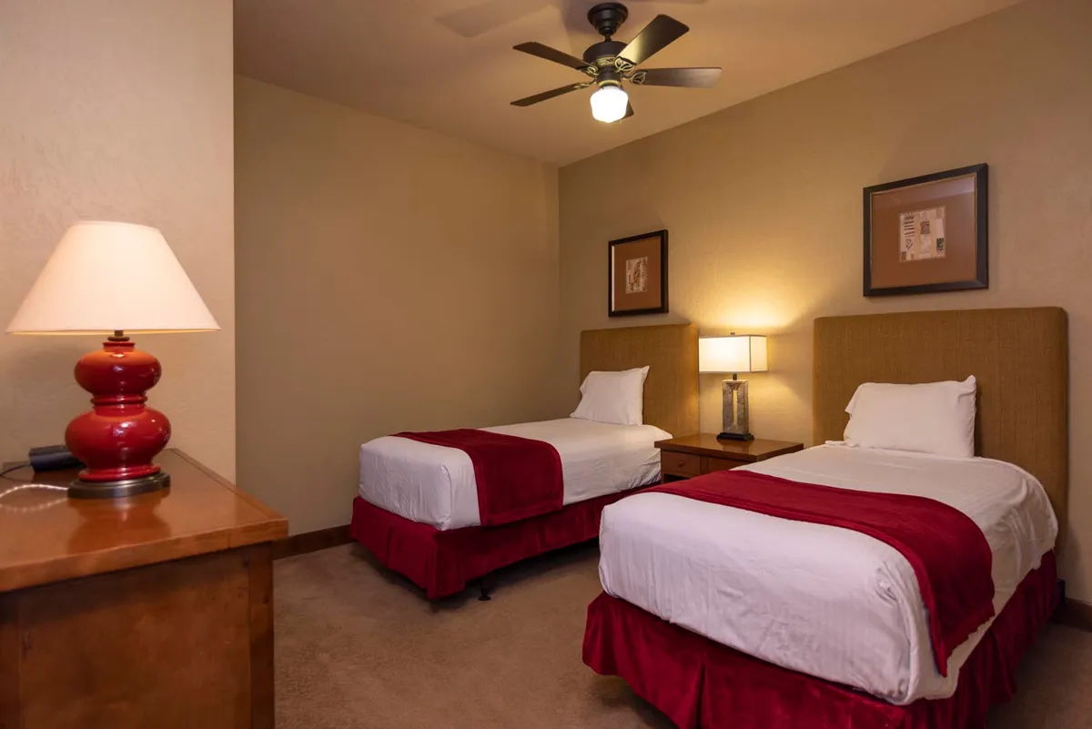 A bright and inviting bedroom with two twin beds, each with crisp linens, cozy throws, and decorative artwork above. Nightstands and lamps add a homely touch, providing a perfect retreat for guests or children.