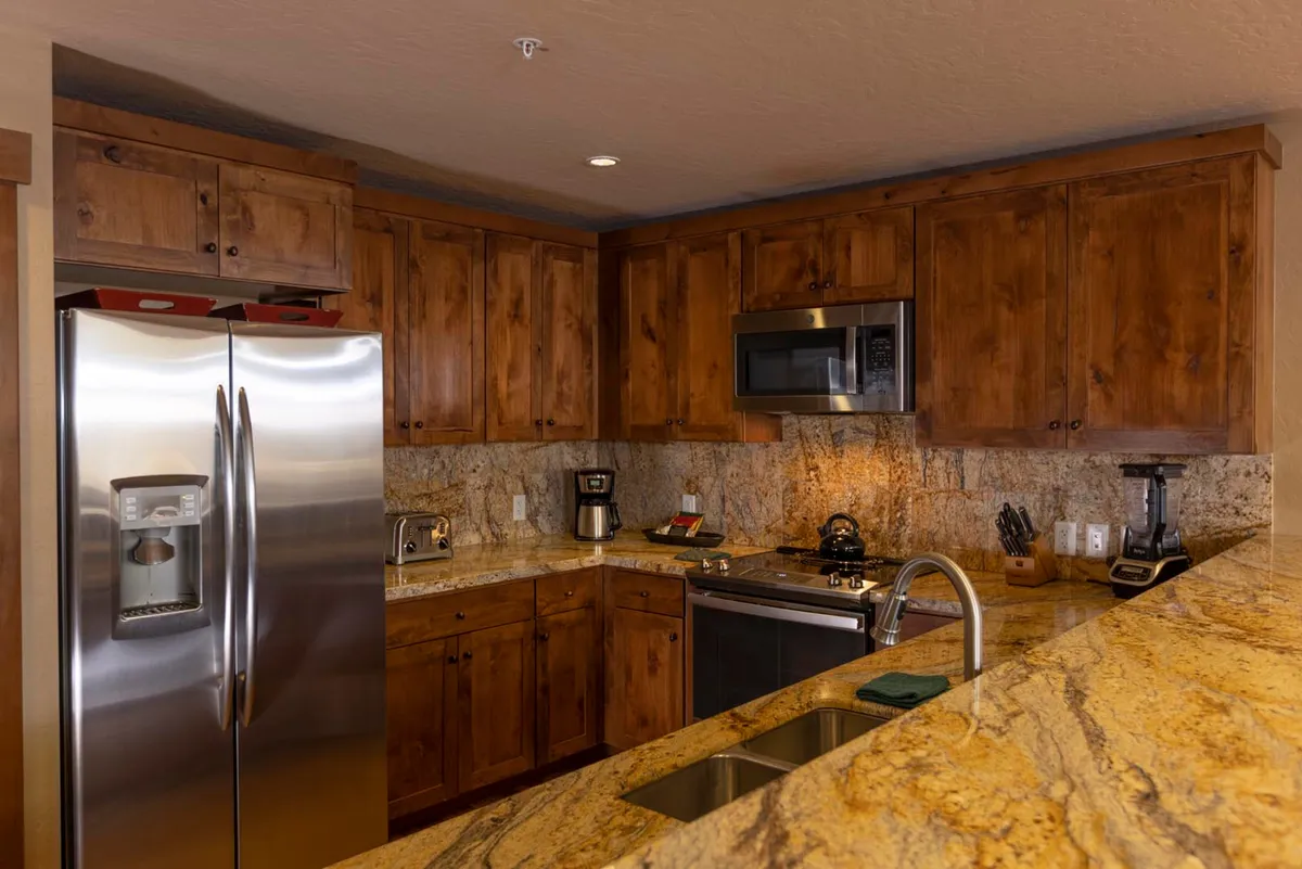 Featuring the stainless steel refrigerator, granite countertops, and wood cabinetry, this cozy kitchen shot captures the heart of the culinary space. The layout makes it easy to prepare group feasts or quick breakfasts, with plenty of room for helpers and guests to gather around.