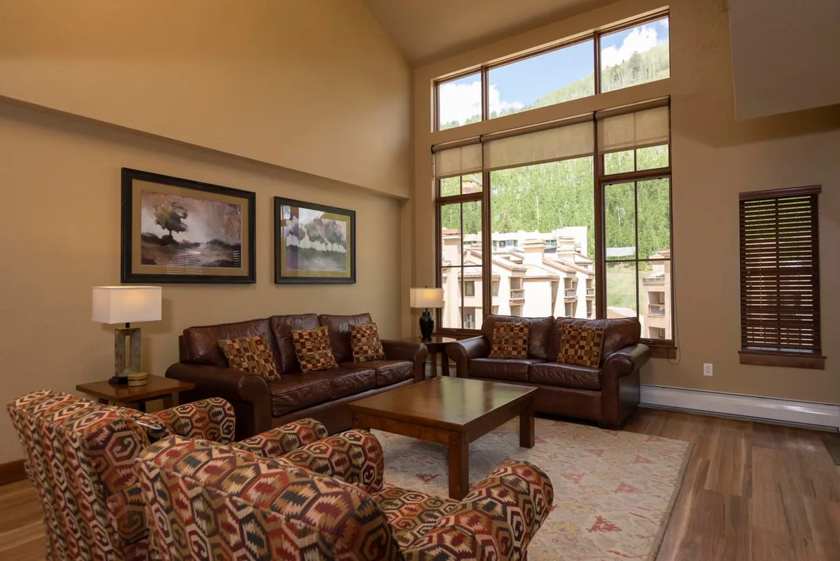 This image highlights a spacious living room filled with natural light. Large panoramic windows frame breathtaking mountain views, while plush seating is arranged around a central wooden coffee table. Decorative artwork adds character to the walls, and the overall atmosphere feels cozy and inviting—perfect for family gatherings or unwinding after outdoor adventures.