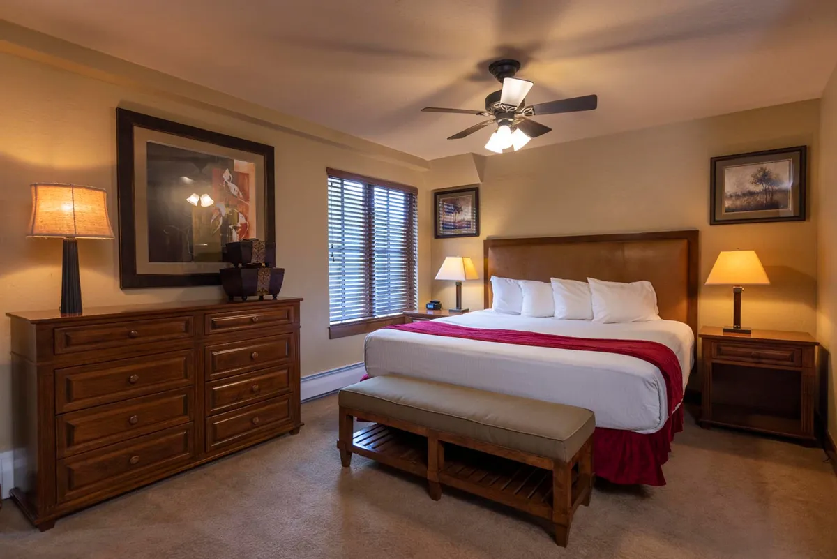 A warmly lit king bedroom featuring a spacious king-size bed, elegant nightstands with lamps, a dresser, and tasteful artwork on the walls. The room exudes comfort and privacy—ideal for relaxation after a long day.