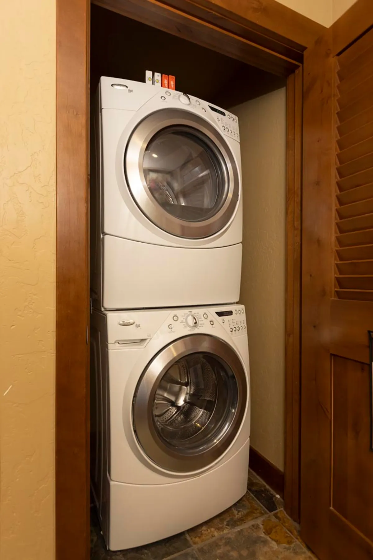 A compact and practical laundry area with a stacked washer and dryer, shelving above for supplies, and a warm wooden door frame. This utility space ensures guests enjoy all the comforts of home.