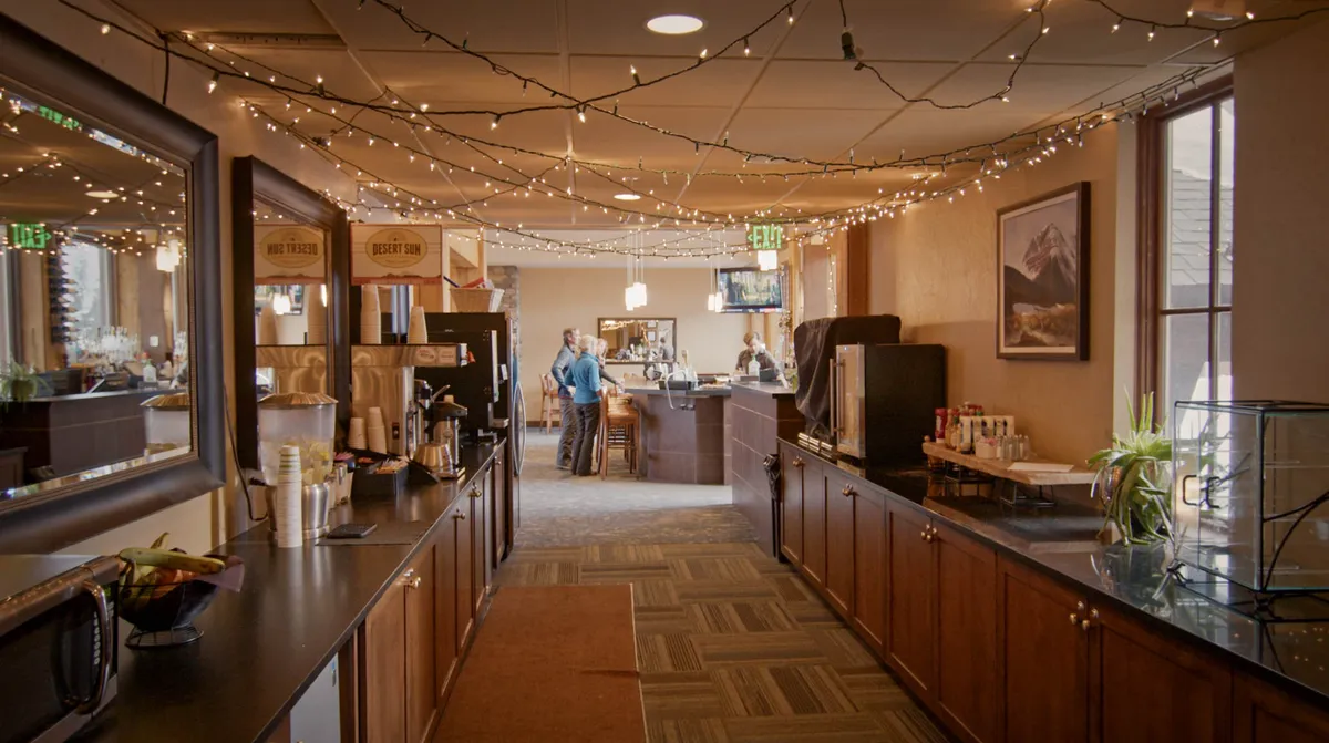 A welcoming interior lounge featuring a coffee station, bar area, decorative lights, and comfortable seating. The space invites guests to relax, socialize, or enjoy refreshments after a day of activities.