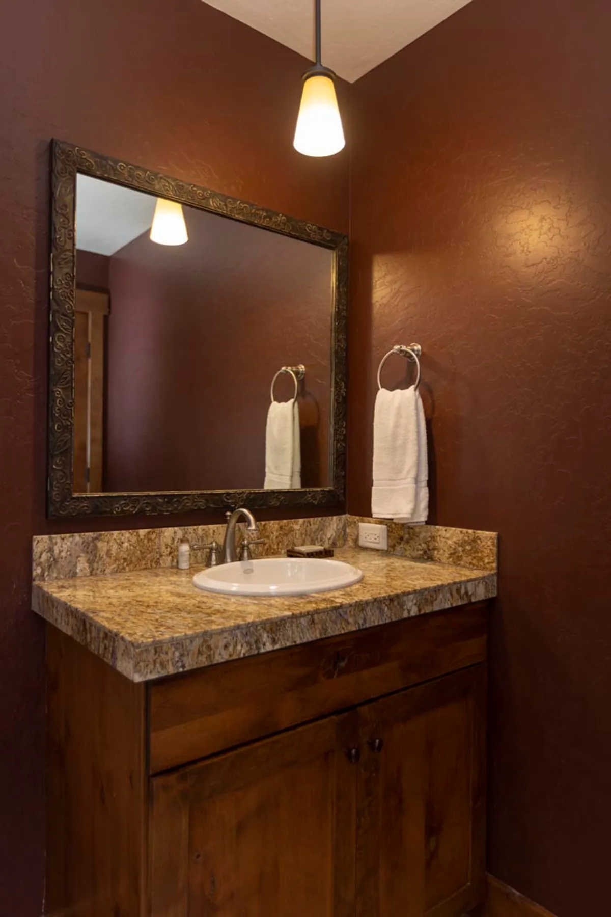 A warmly lit bathroom interior with a granite countertop, ornate mirror, and modern faucet. The inviting space hints at moments of self-care and relaxation, with an atmosphere that aligns with spa treatments or morning rituals.